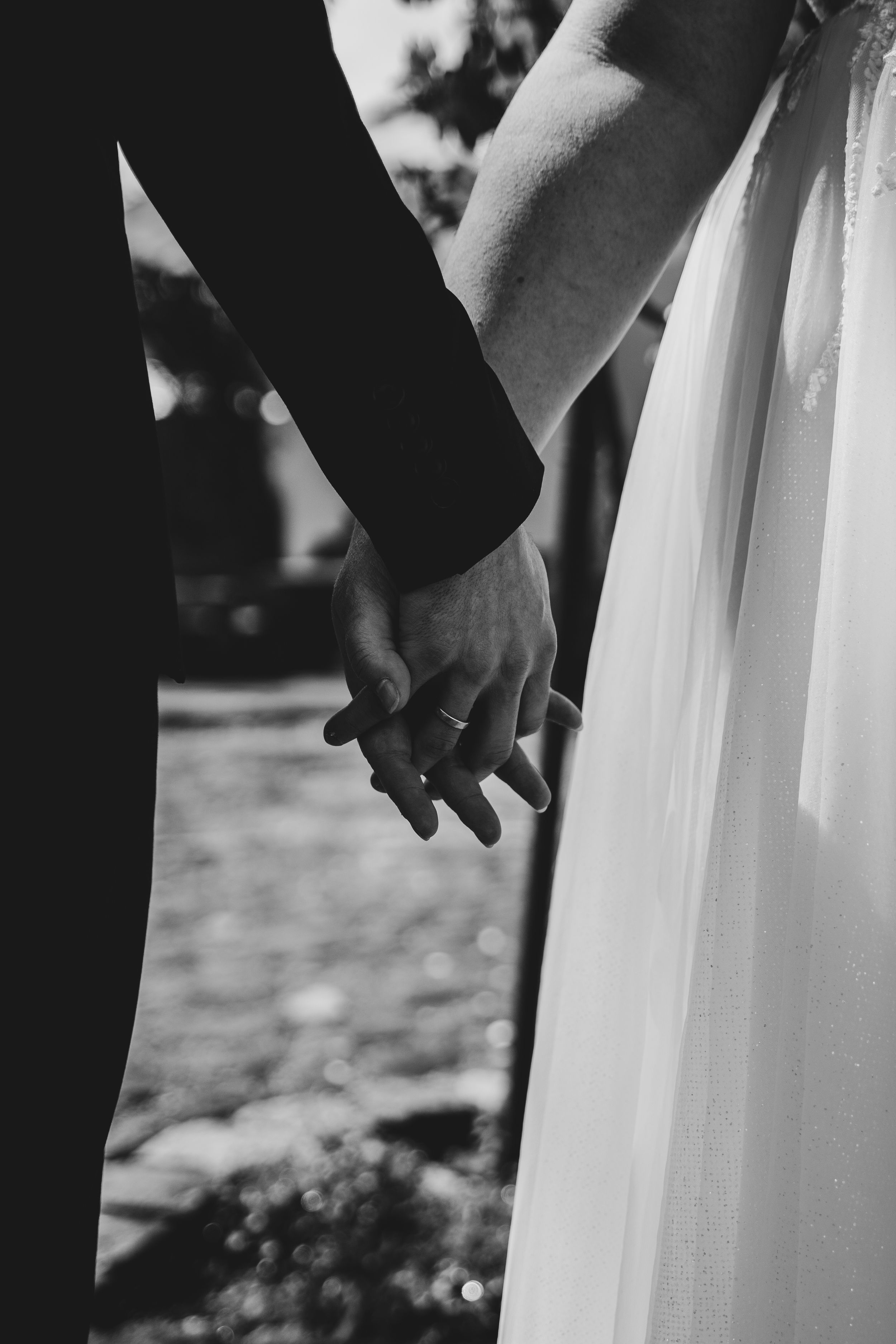 Black and white detail shot of couple holding hands during wedding ceremony.