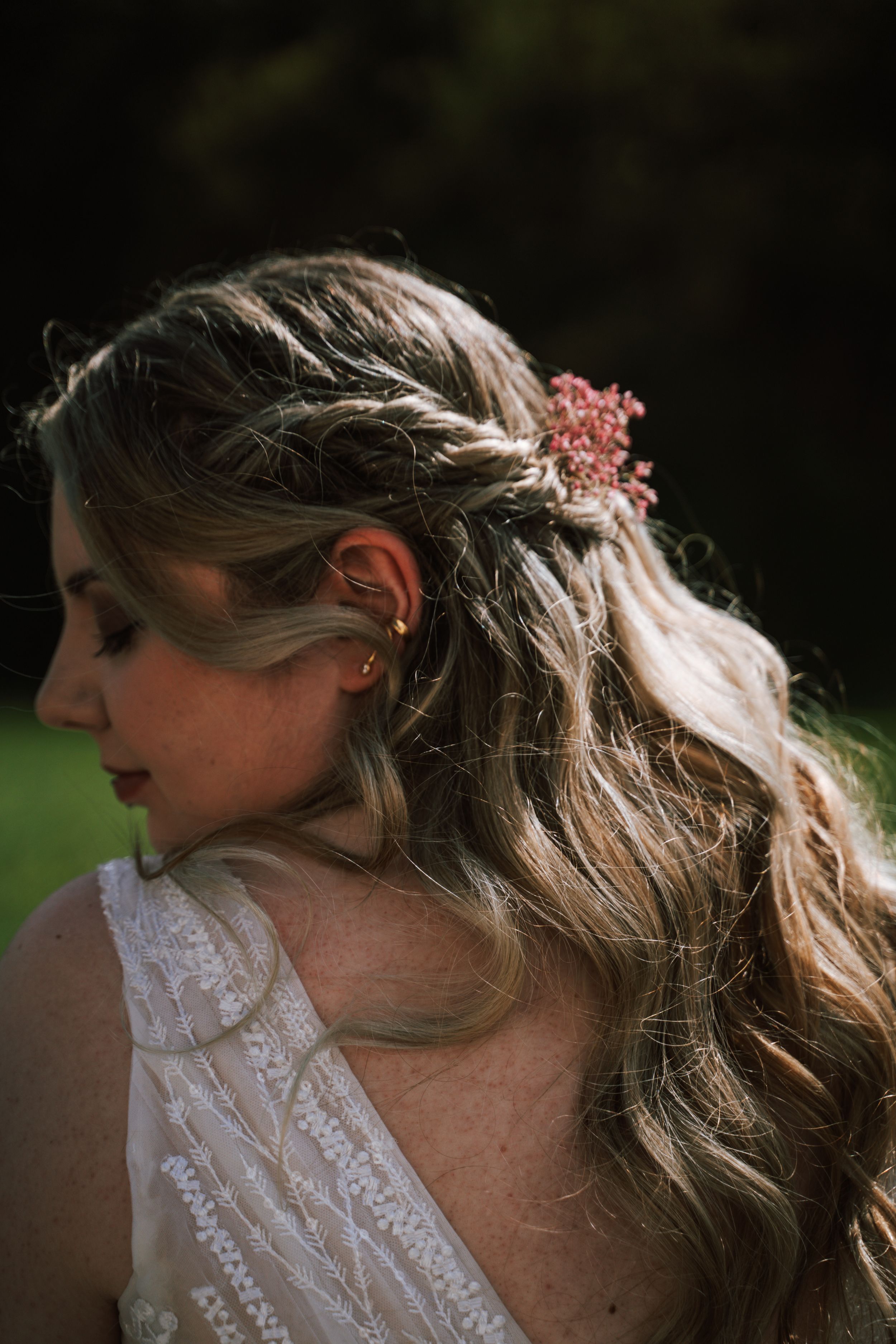 Side profile of bridal hairstyle with floral accessories against natural backdrop.