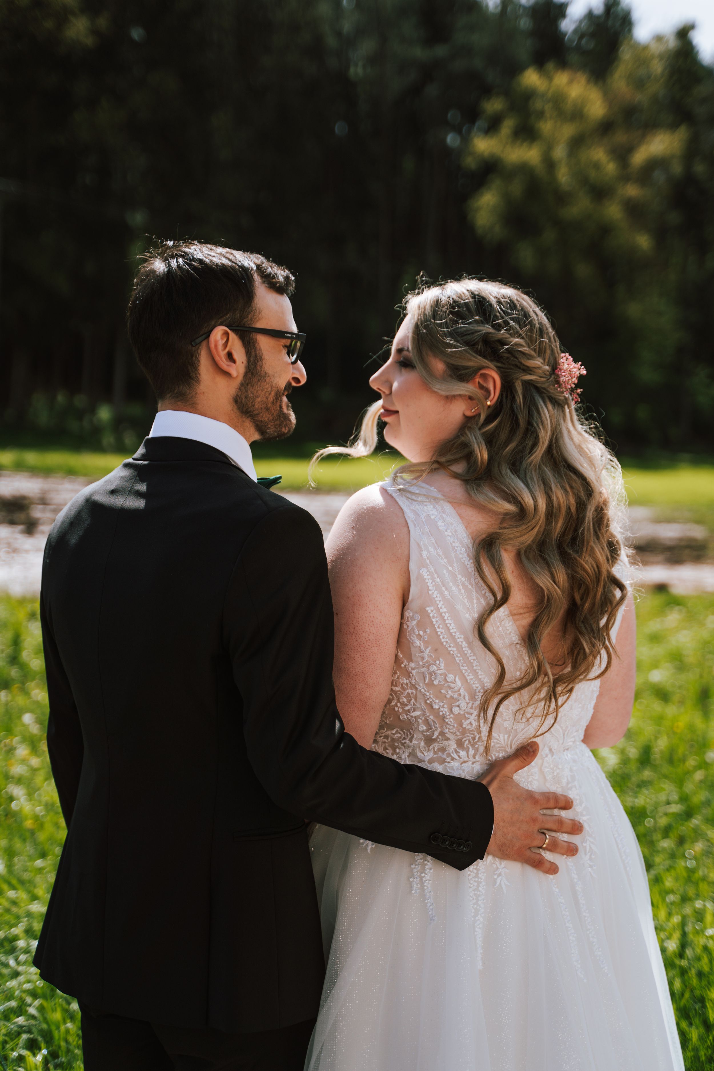 A romantic wedding portrait of a couple embracing outdoors with the bride in a lace dress and groom in a black suit.