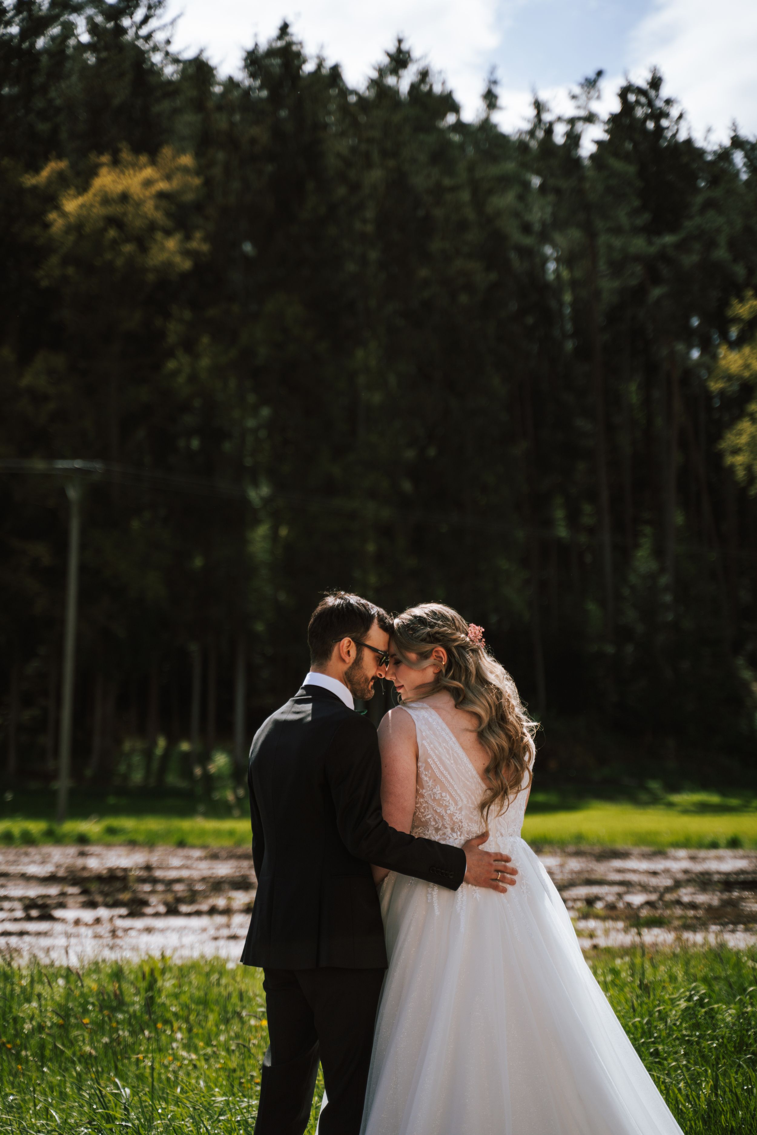 Wedding couple embraces in front of a pine forest on their special day.