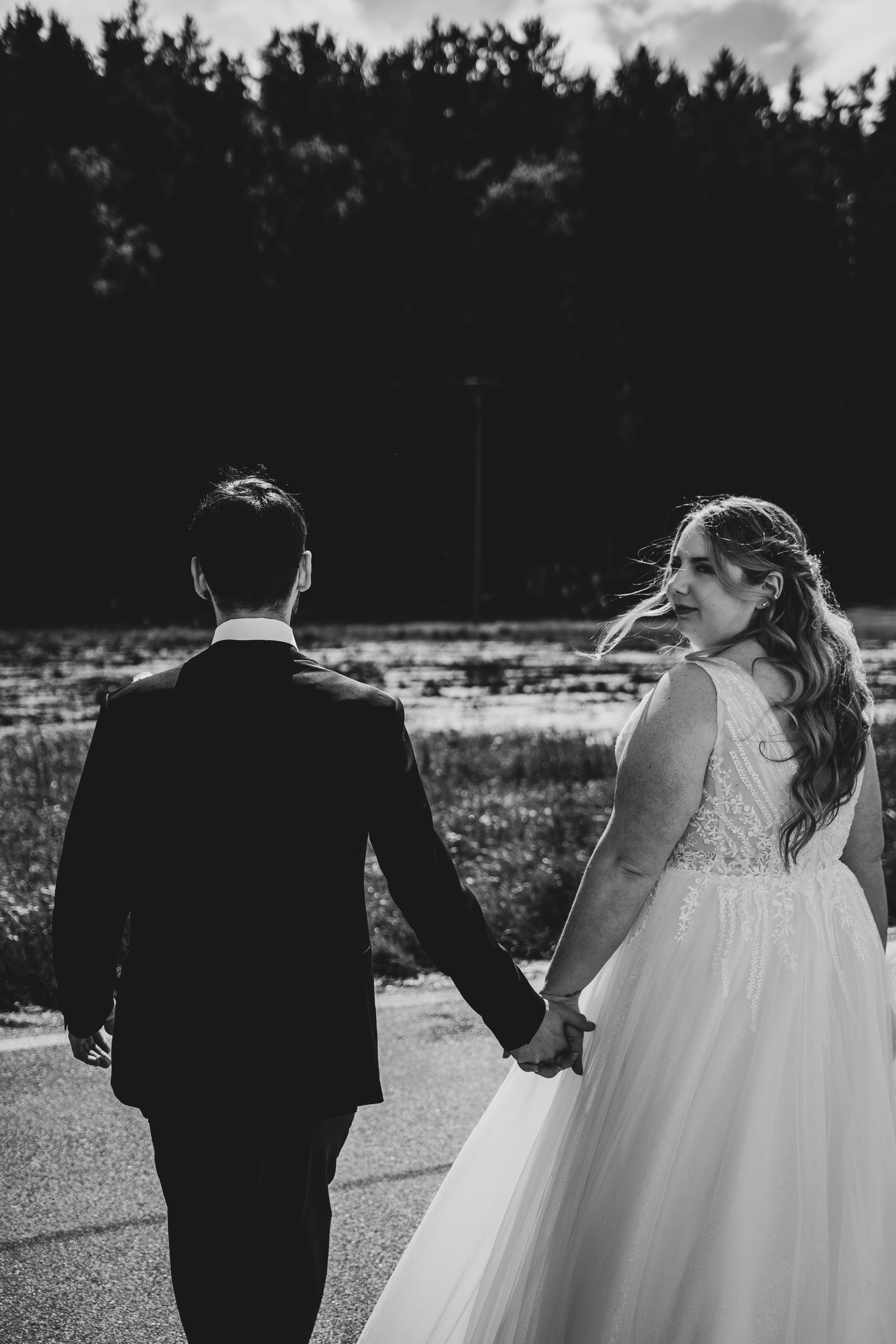 Black and white portrait of newlyweds walking hand in hand along a path.