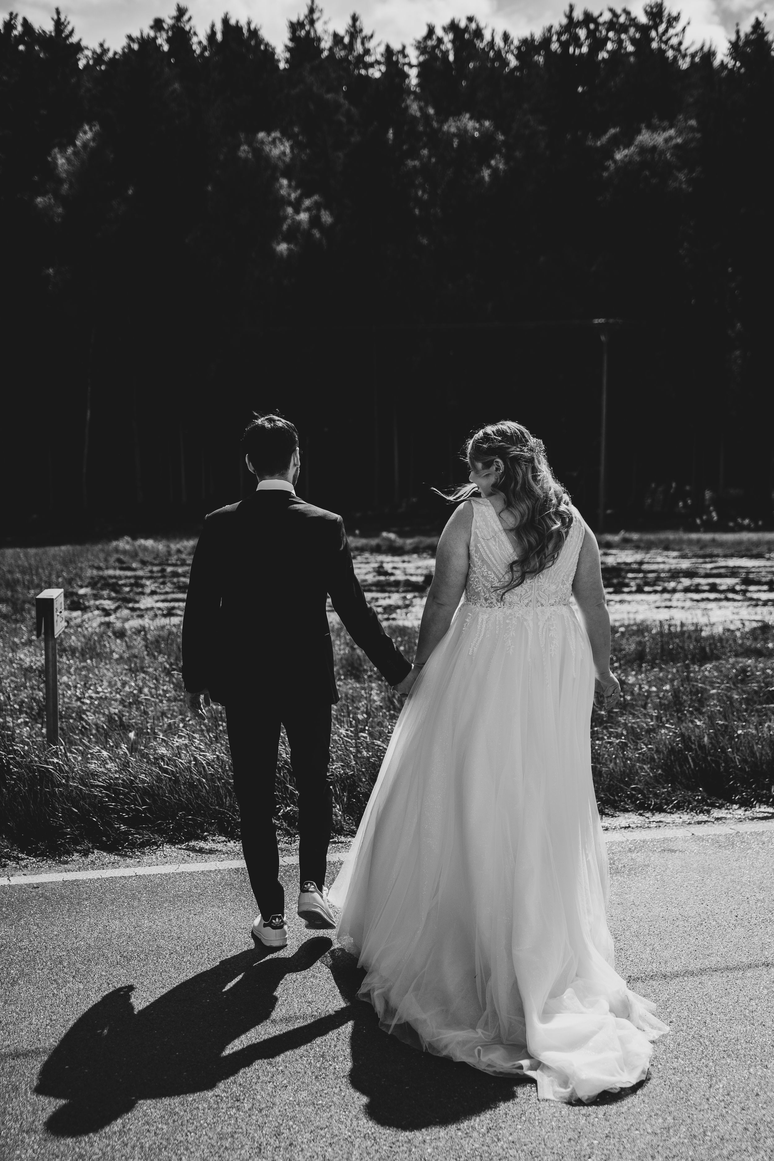 Black and white image of newlyweds walking together casting long shadows.