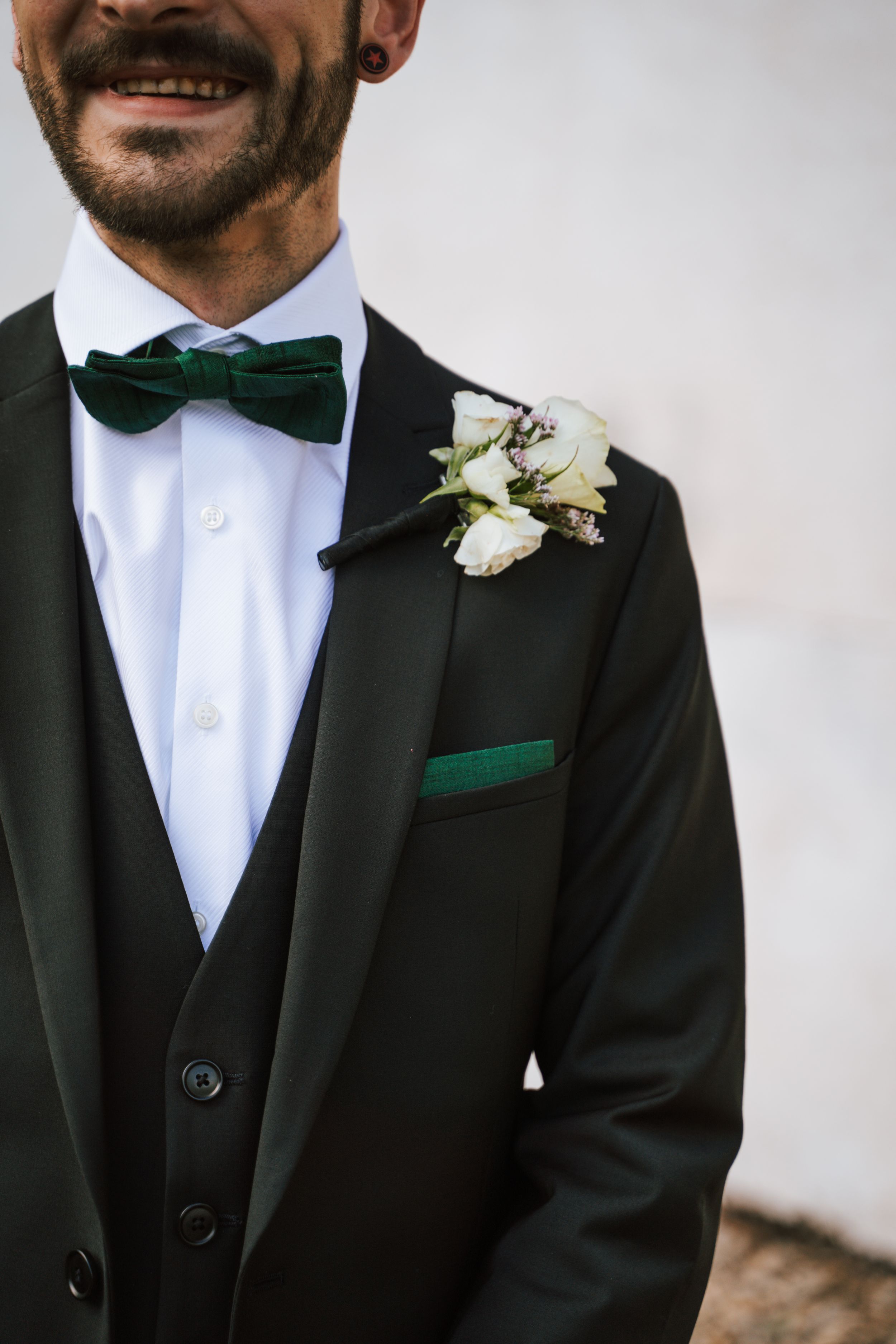 Detail shot of black tuxedo with green bow tie and white boutonniere.