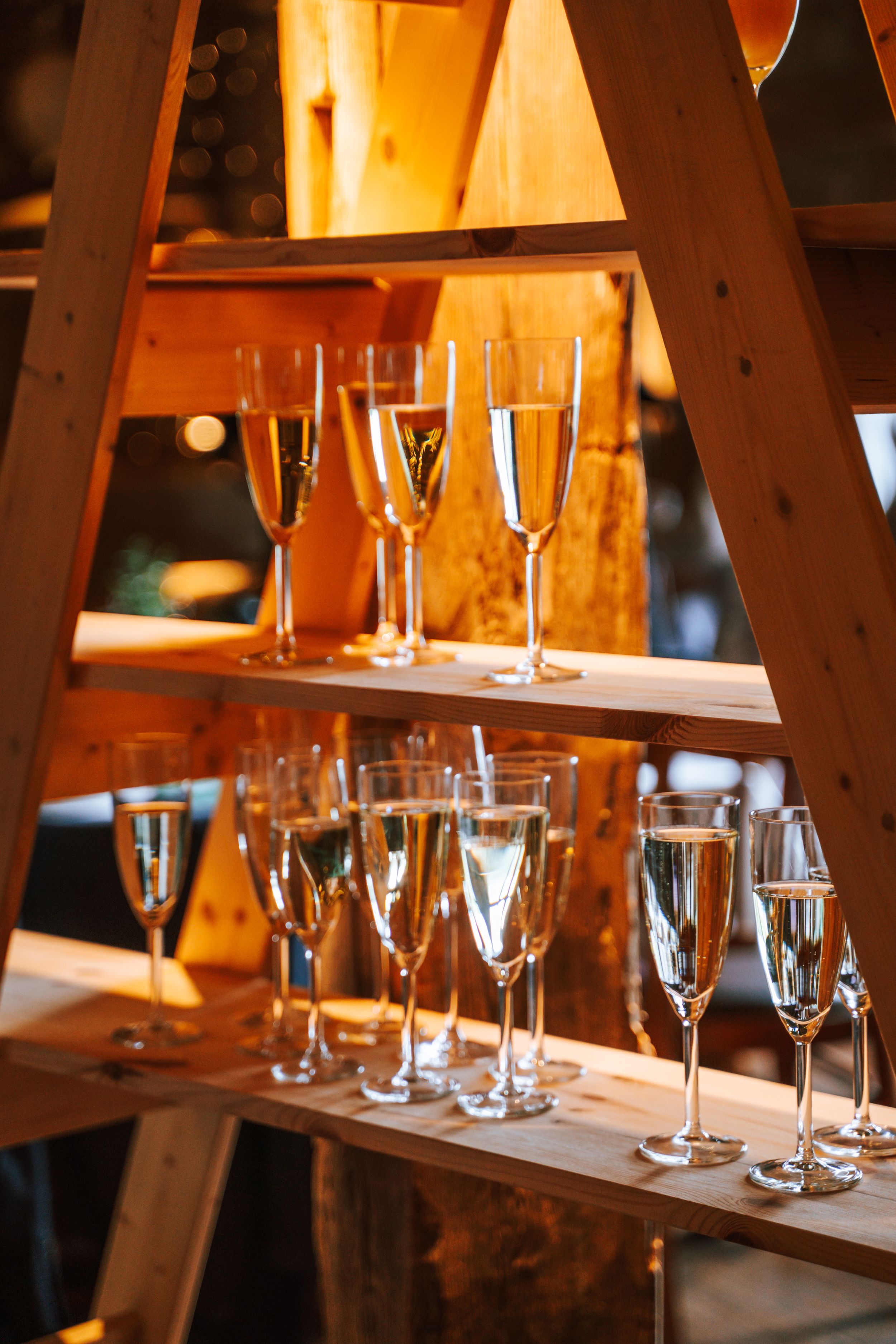 Wine glasses arranged on wooden shelves in warm lighting create an elegant display at a wedding reception.