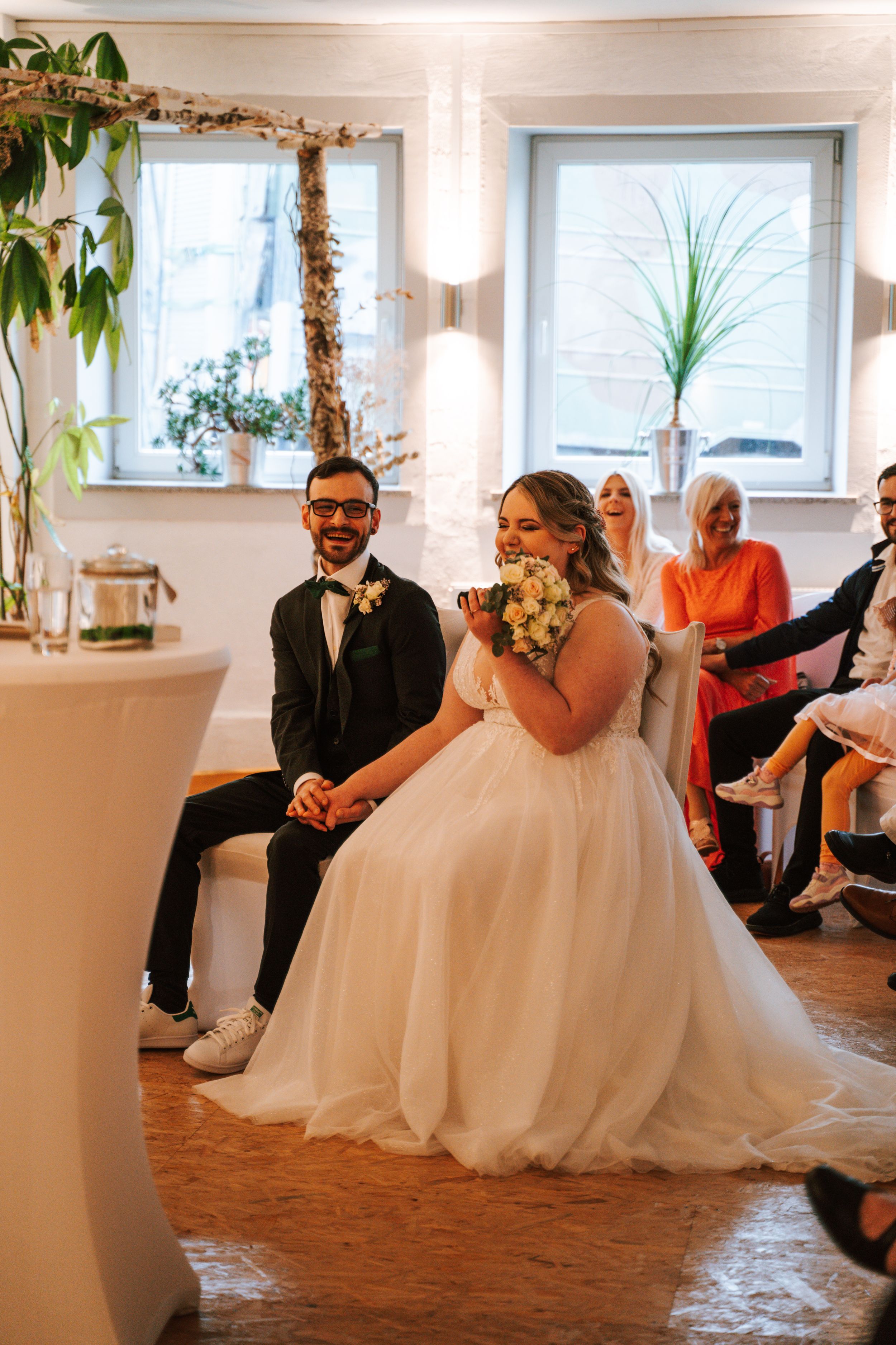 Wedding party seated in a modern venue with natural light streaming through windows.