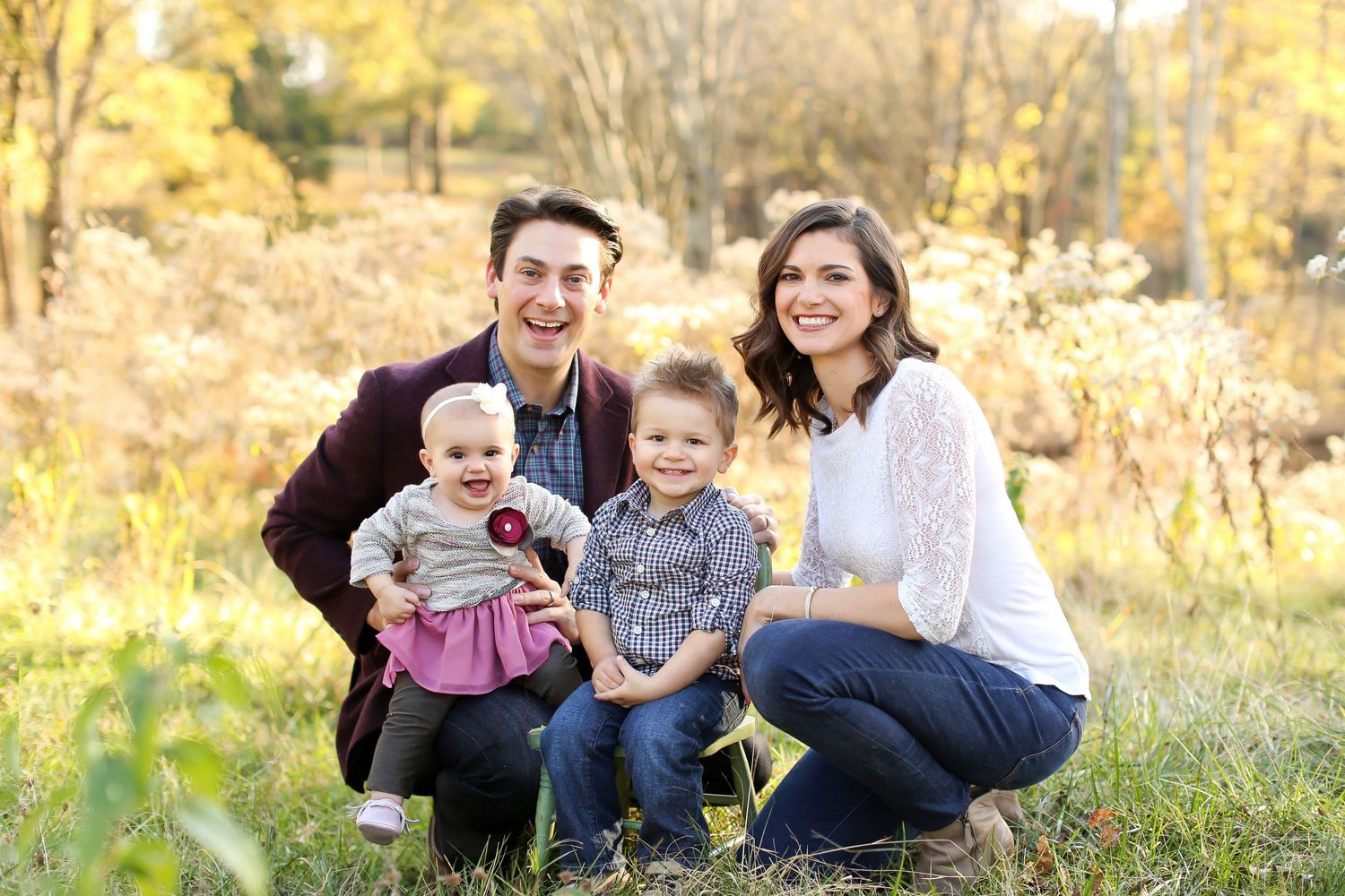 Family sitting together in fall field with golden foliage background.