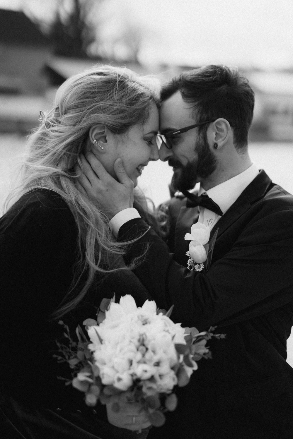 A black and white portrait of a couple sharing an intimate moment with a white bouquet.