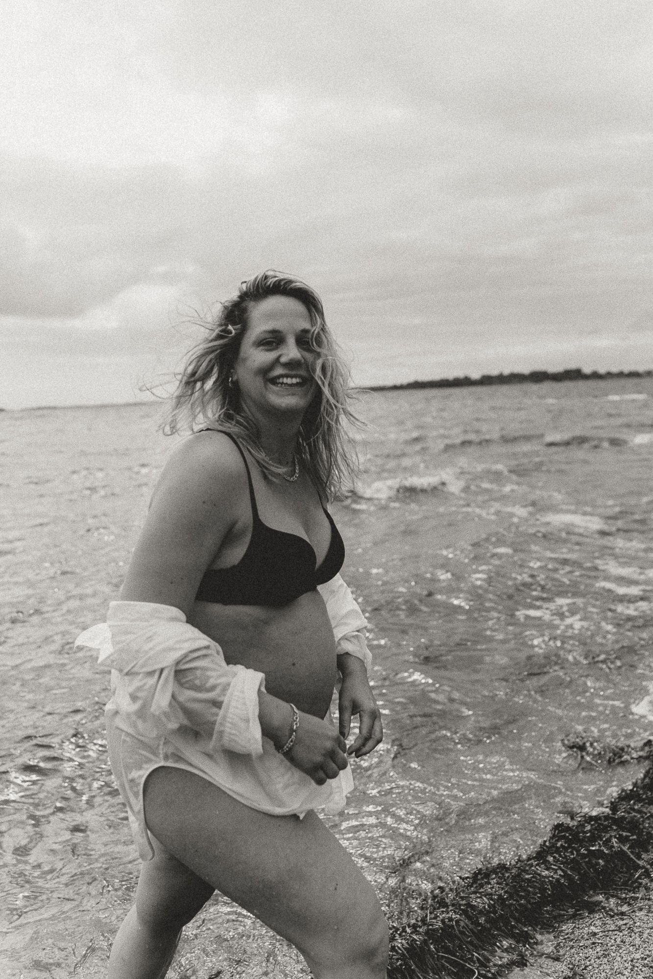 A joyful figure splashes in the ocean waves wearing black swimwear and a white shirt.