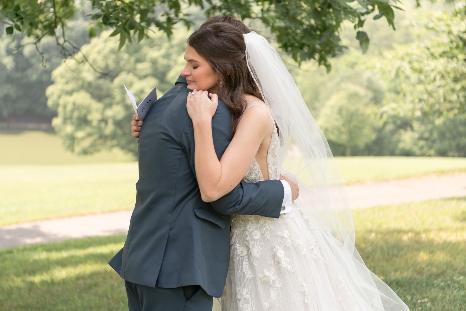 Romantic embrace between couple in wedding attire against sunny outdoor backdrop.