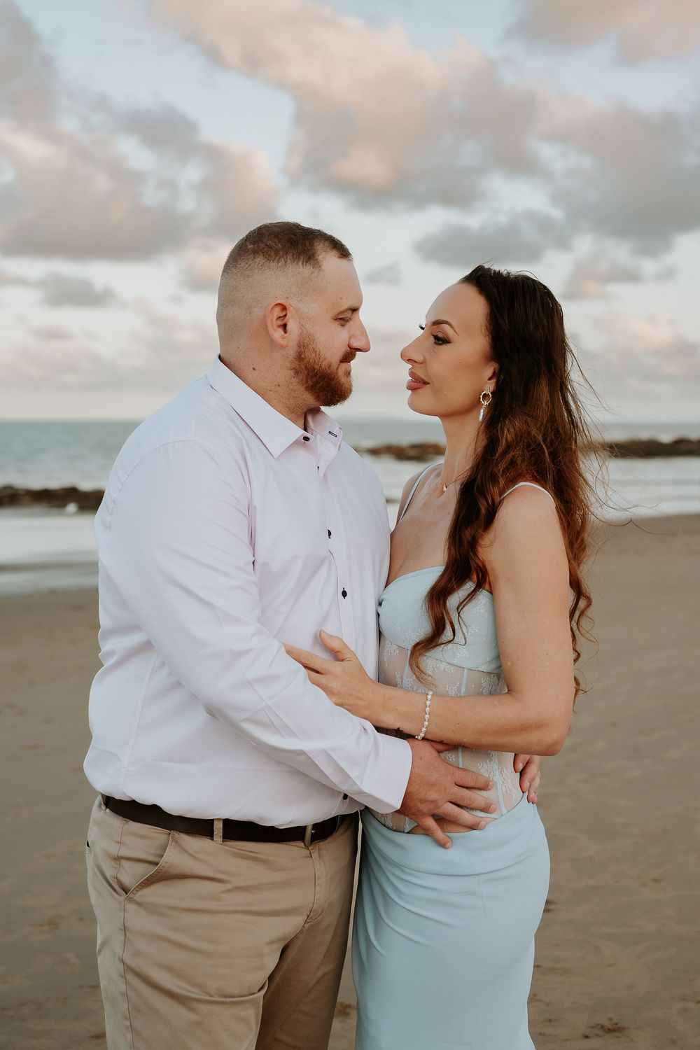 Couple in formal attire embracing on tannum sands beach during sunset.