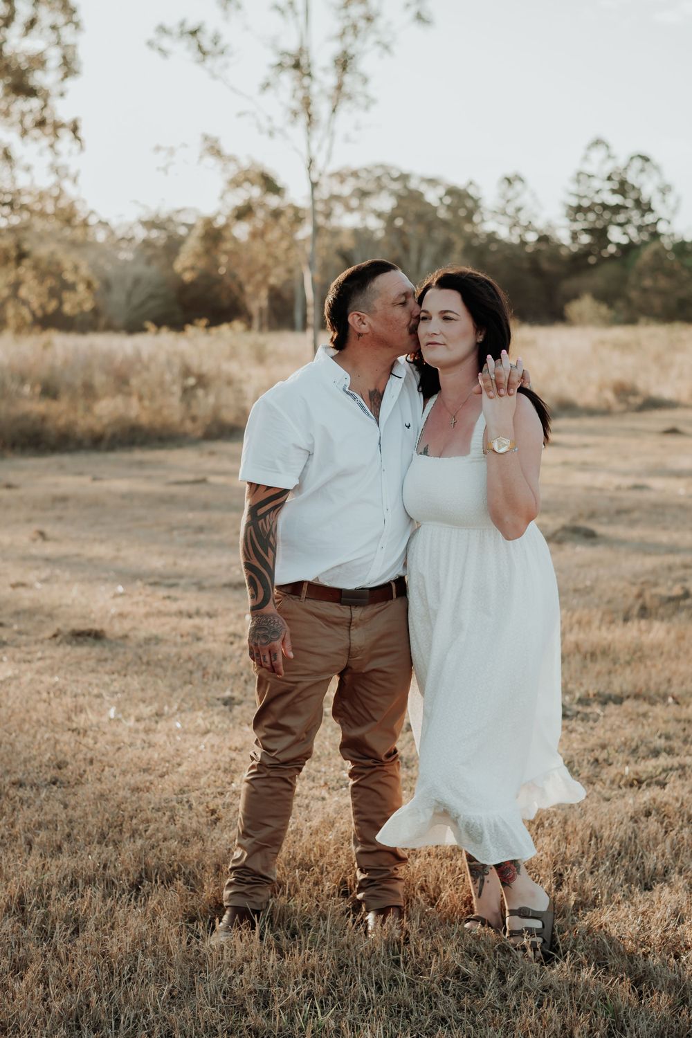 Couple in white and brown outfits embraces in rustic calliope field.