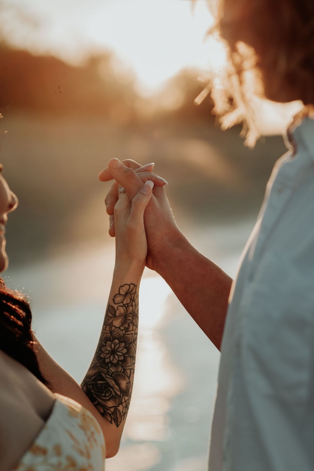 Close-up of tattooed hands holding each other against sunset backdrop.