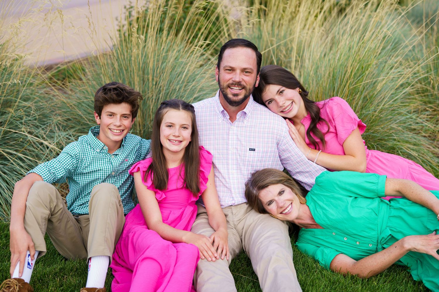 A family in colorful coordinated outfits sits together against ornamental grass.