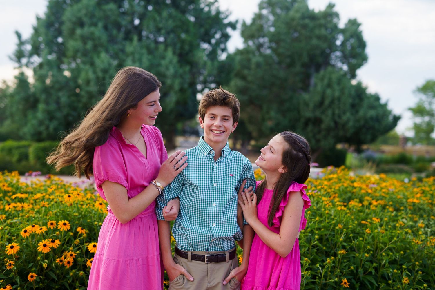 Three people in bright coordinated outfits laugh together in a flower garden.