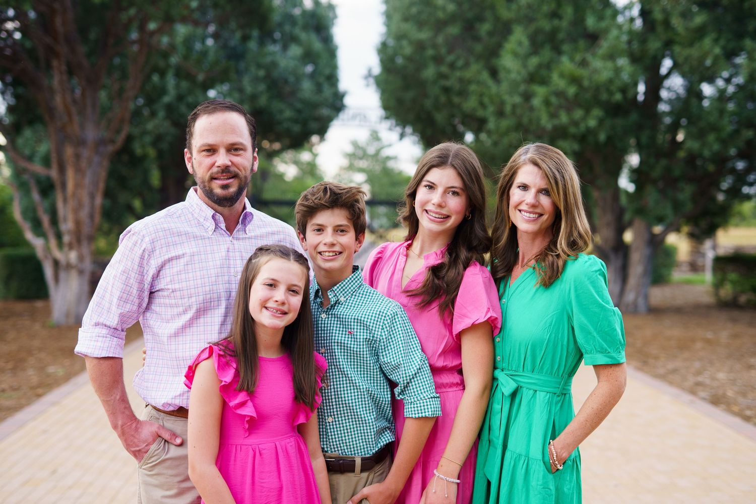 A family in pink and green coordinated outfits smiles together outdoors.