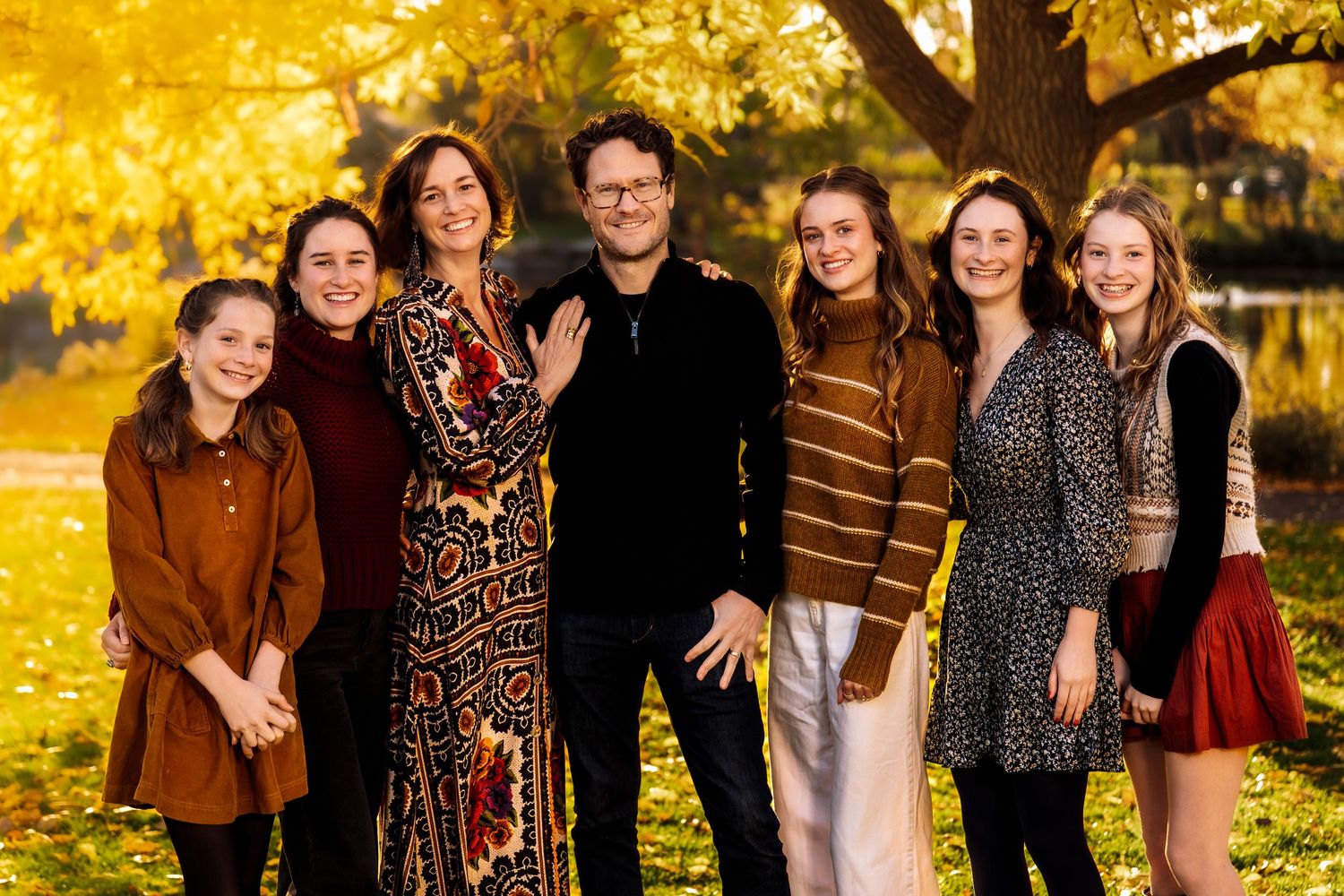 A group of people pose together outdoors during autumn with golden yellow foliage in the background.