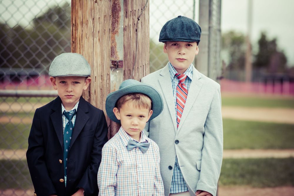 Three young boys wearing vintage-style caps and suits pose together outdoors.