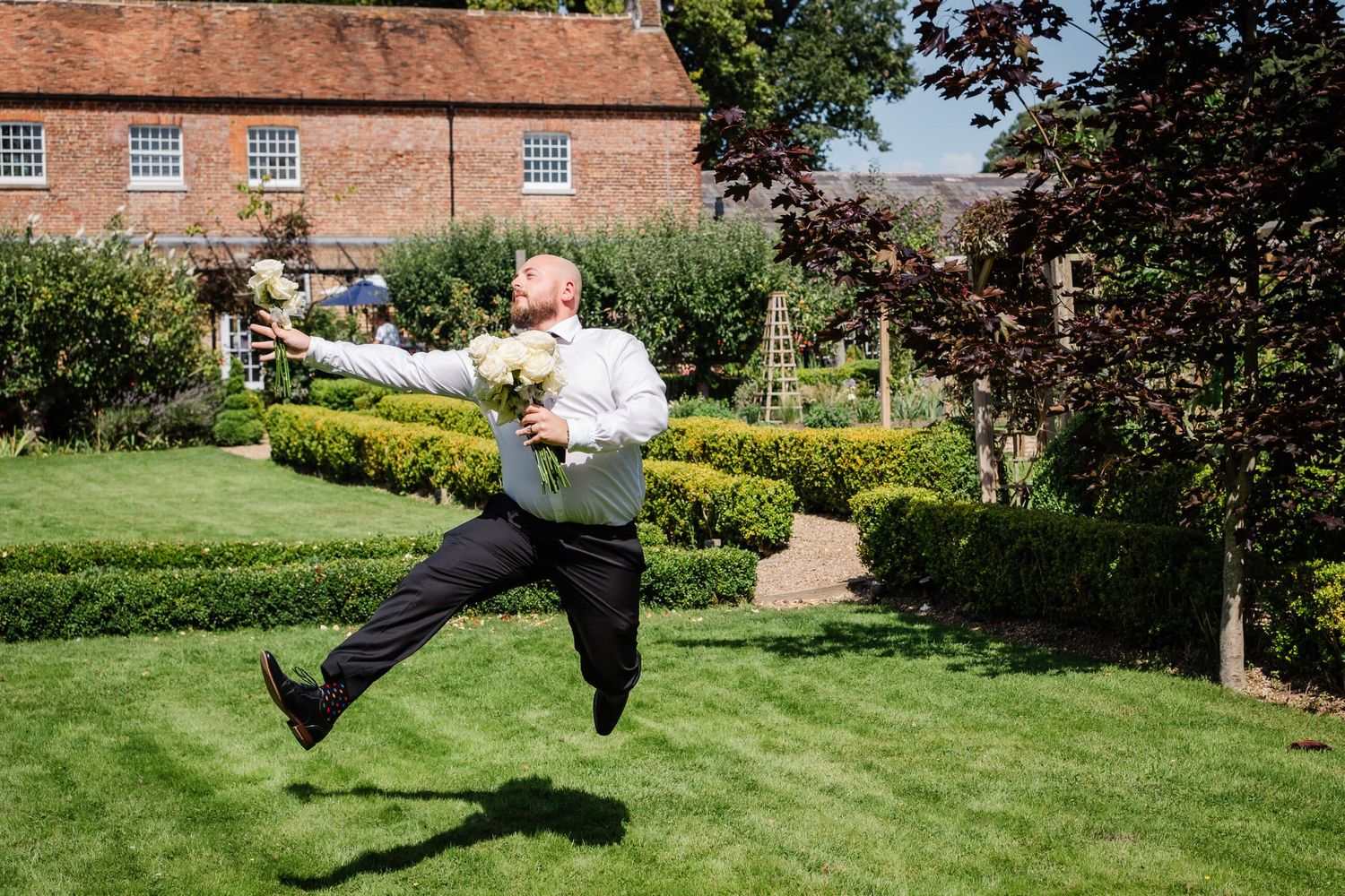 groomsman with wedding flowers jumping at the secret garden ashford wedding venue in Kent