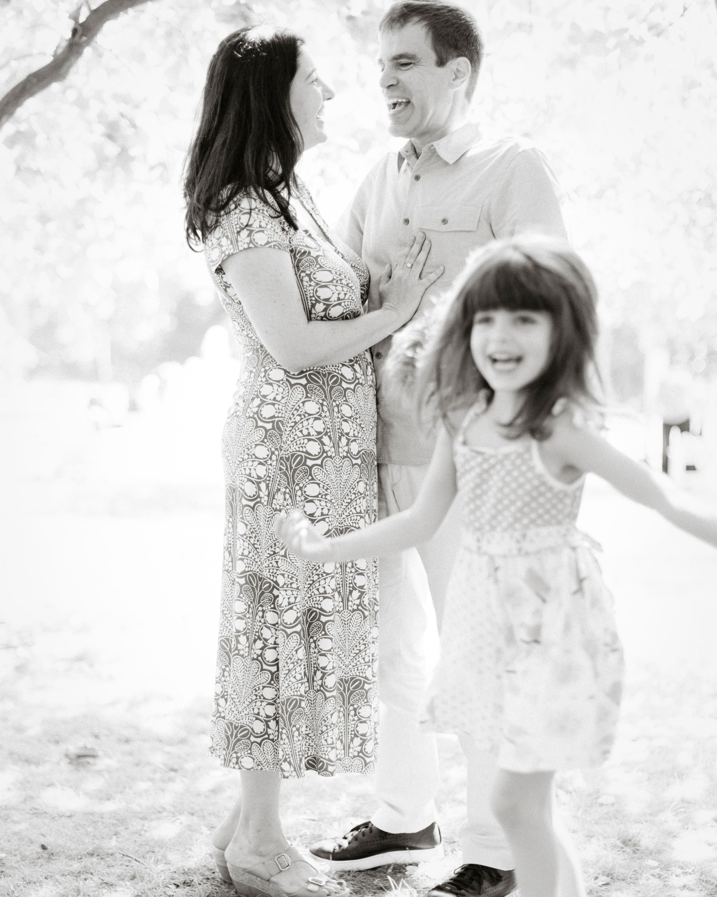 A candid black and white family moment filled with laughter and movement outdoors.