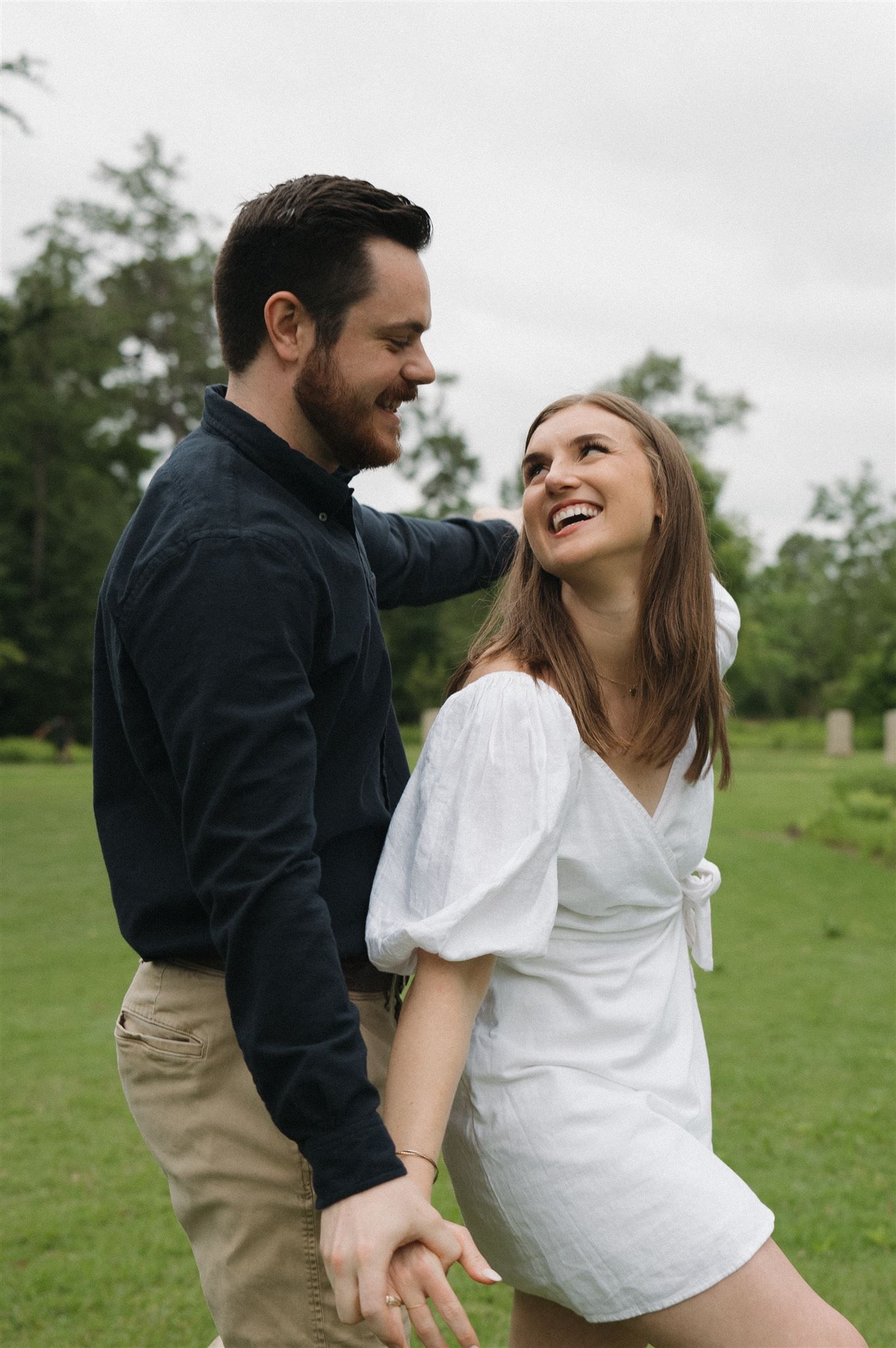 A couple shares a joyful moment together while standing in a green field on an overcast day.