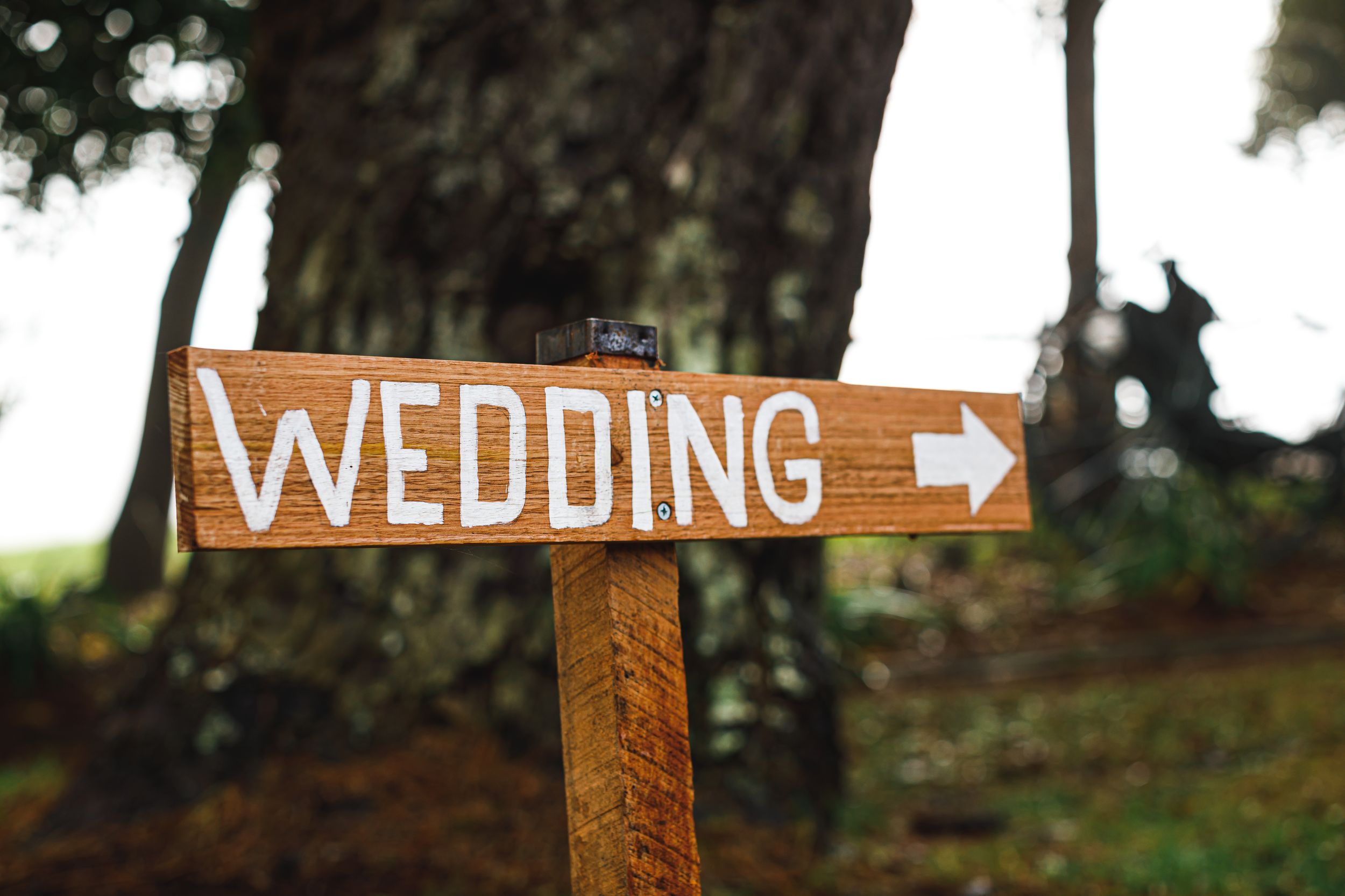 Wooden directional sign with 'WEDDING' text and arrow mounted on post.