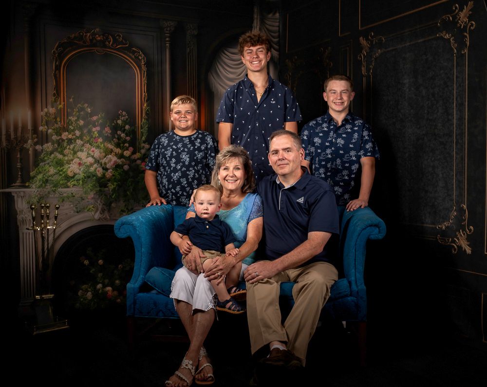 Family portrait series on blue couch against dark elegant backdrop.