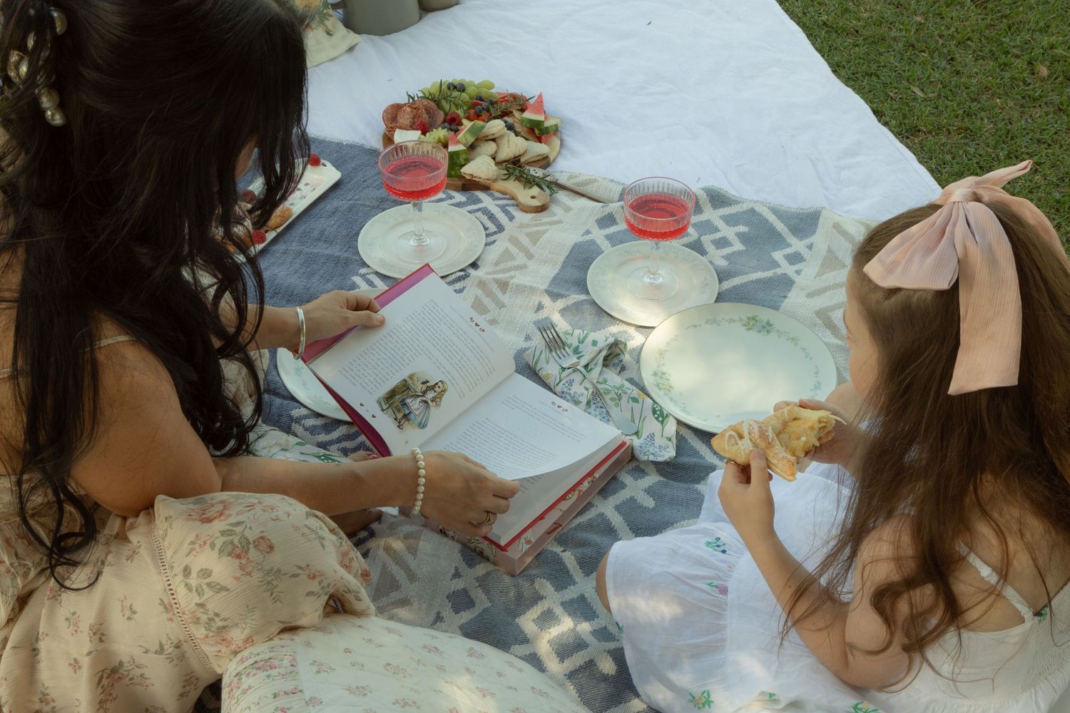 Mother and daughter enjoy an outdoor picnic with refreshments spread on a white blanket.