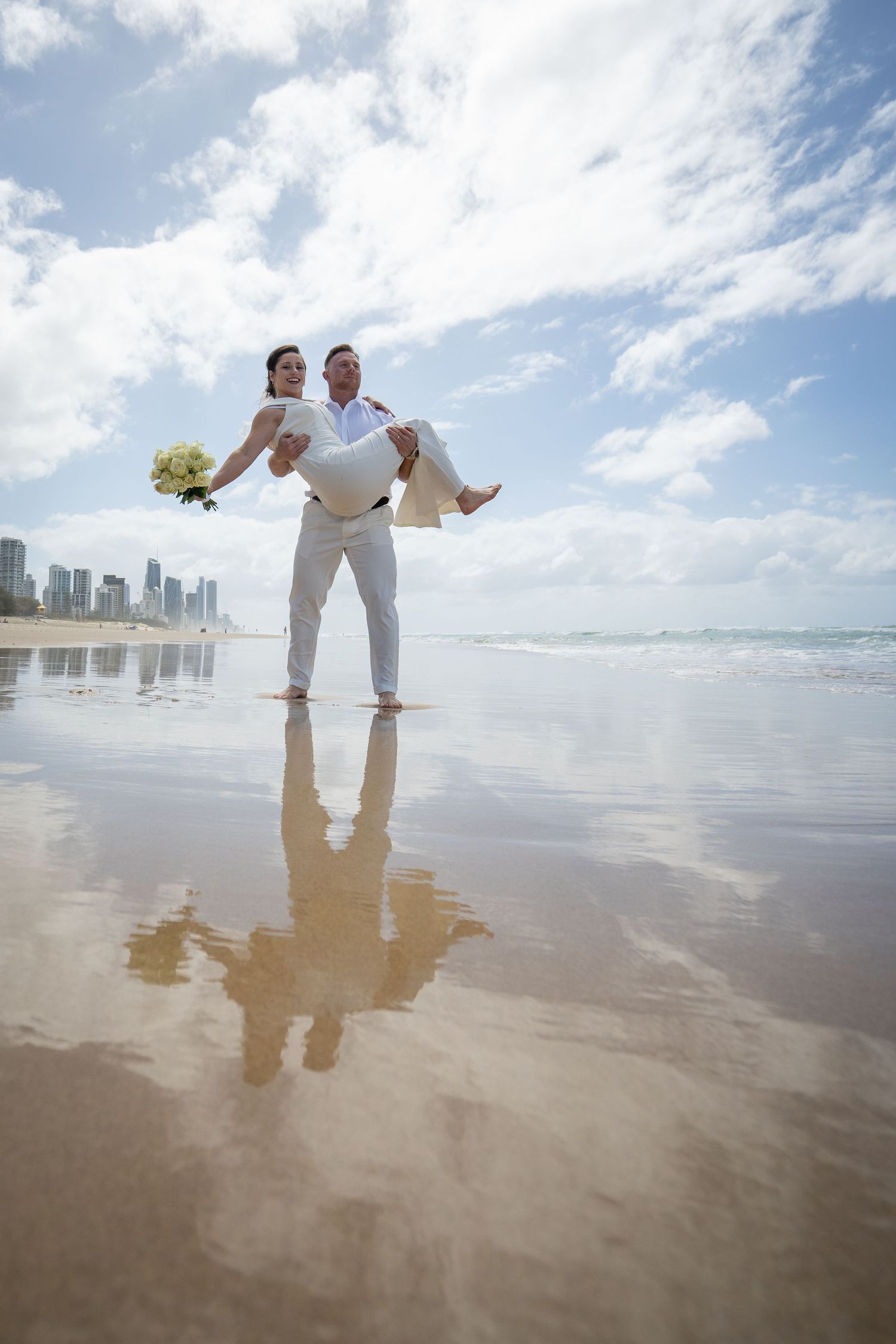 Beach wedding photography sequence with city skyline and reflective wet sand.