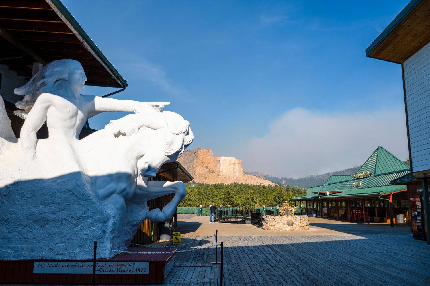 Large white sculpture stands at entrance of outdoor venue with mountains in background under blue sky.