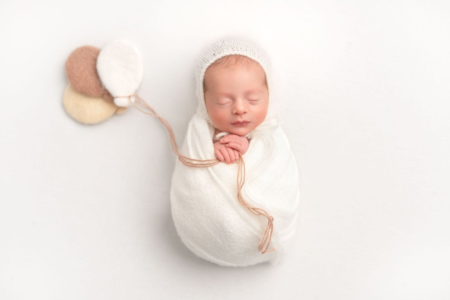 A sleeping newborn swaddled in white lies peacefully on a soft backdrop with a wooden crescent moon prop.