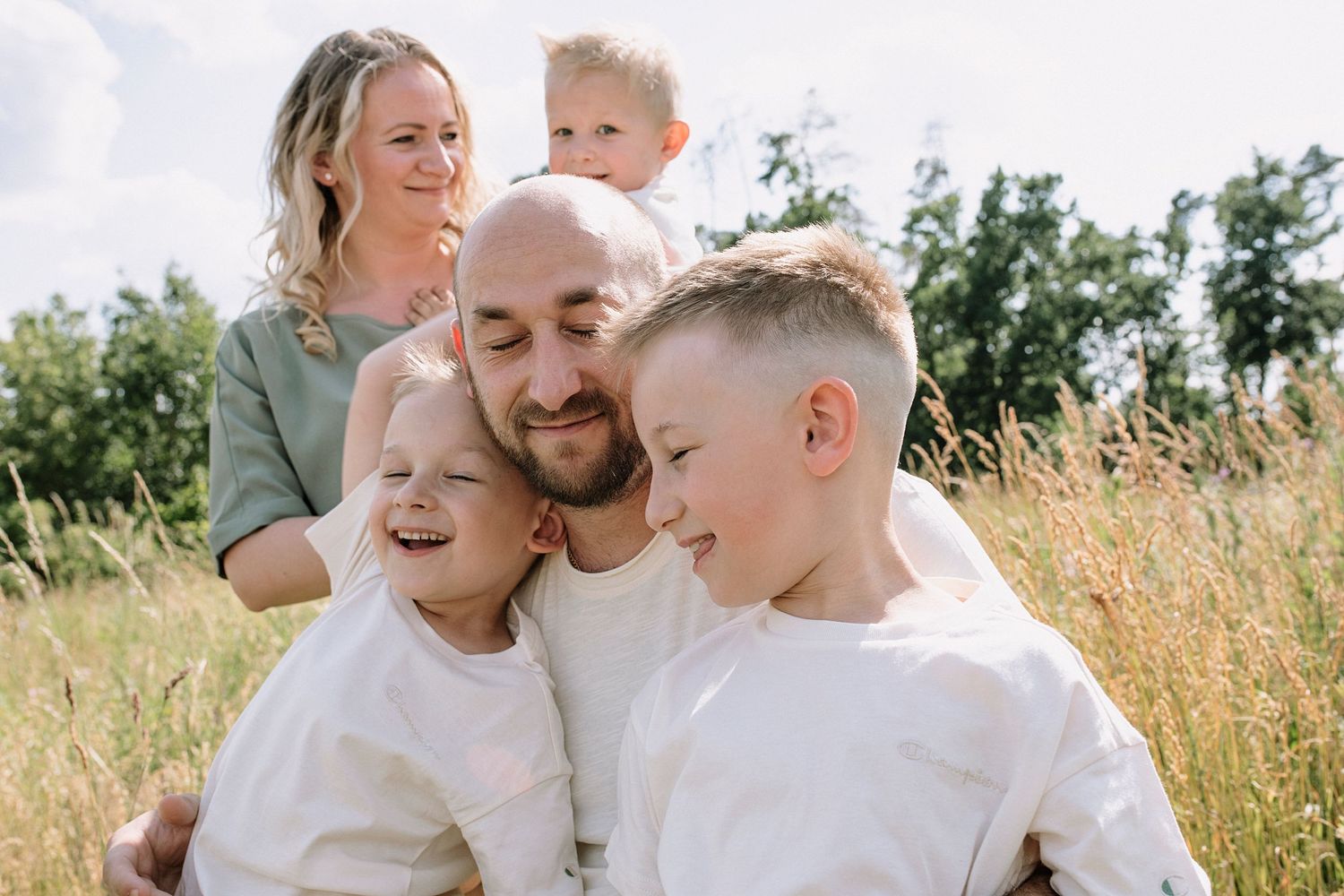 Candid family photo showing joyful interaction in a sunlit meadow setting.