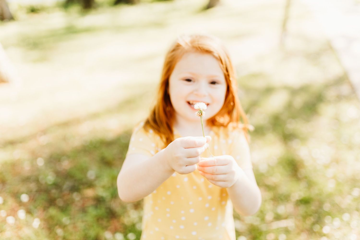 a little redhead girl holds a flower to the camera