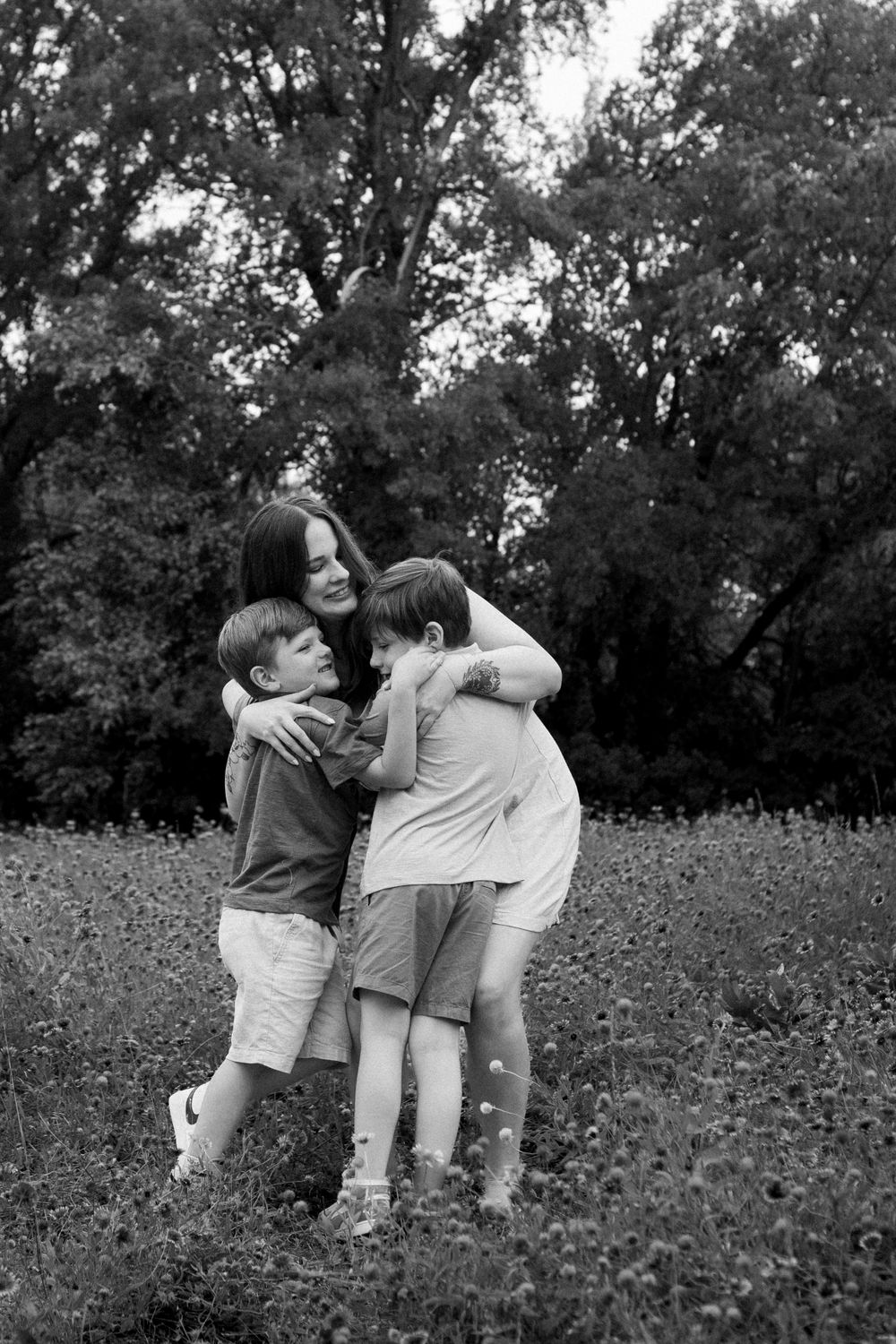 Black and white capture of family embracing and laughing in outdoor field.