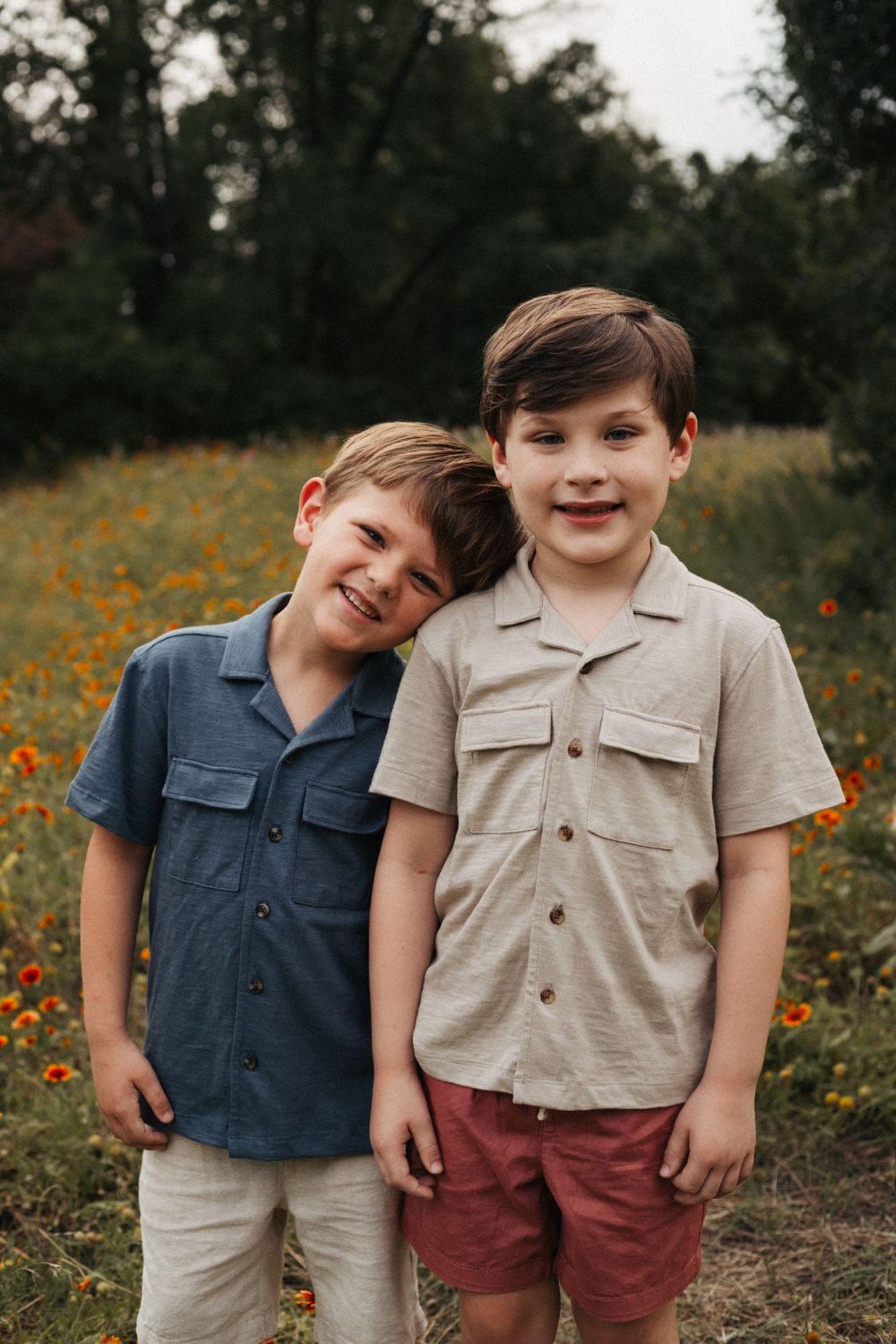Two young boys in matching style shirts smiling in a field of wildflowers.