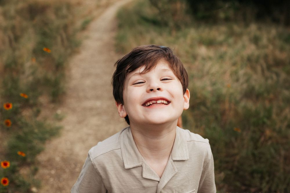 Close-up of child in beige shirt laughing joyfully on a nature path.