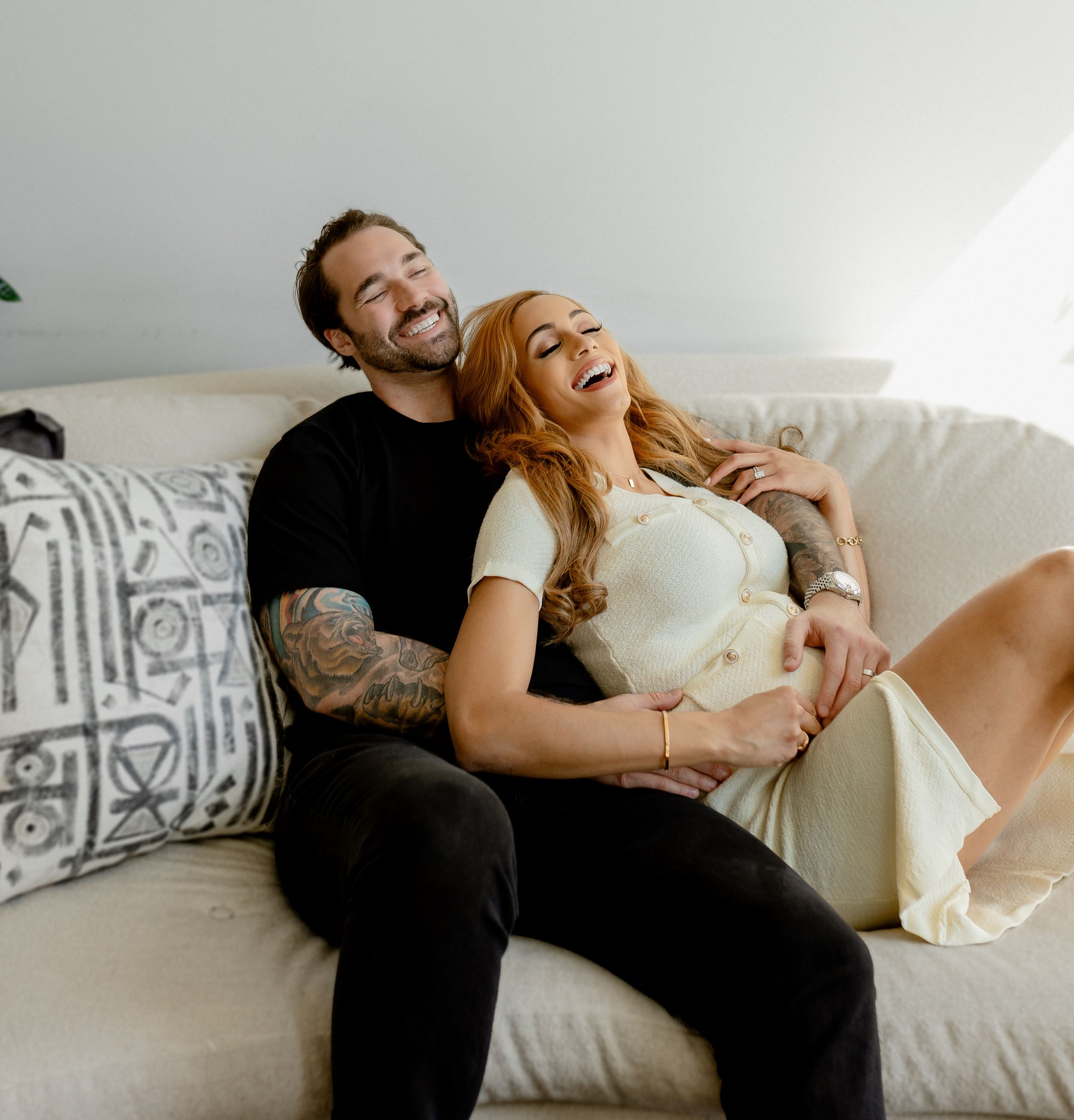 Joyful maternity photo of couple relaxing together on white couch.