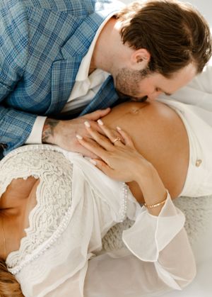 Intimate maternity photo of couple in blue plaid and white lace sharing tender moment.