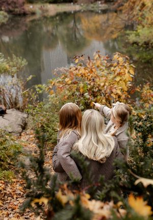 Three people sit on rocks by a pond surrounded by fall foliage.
