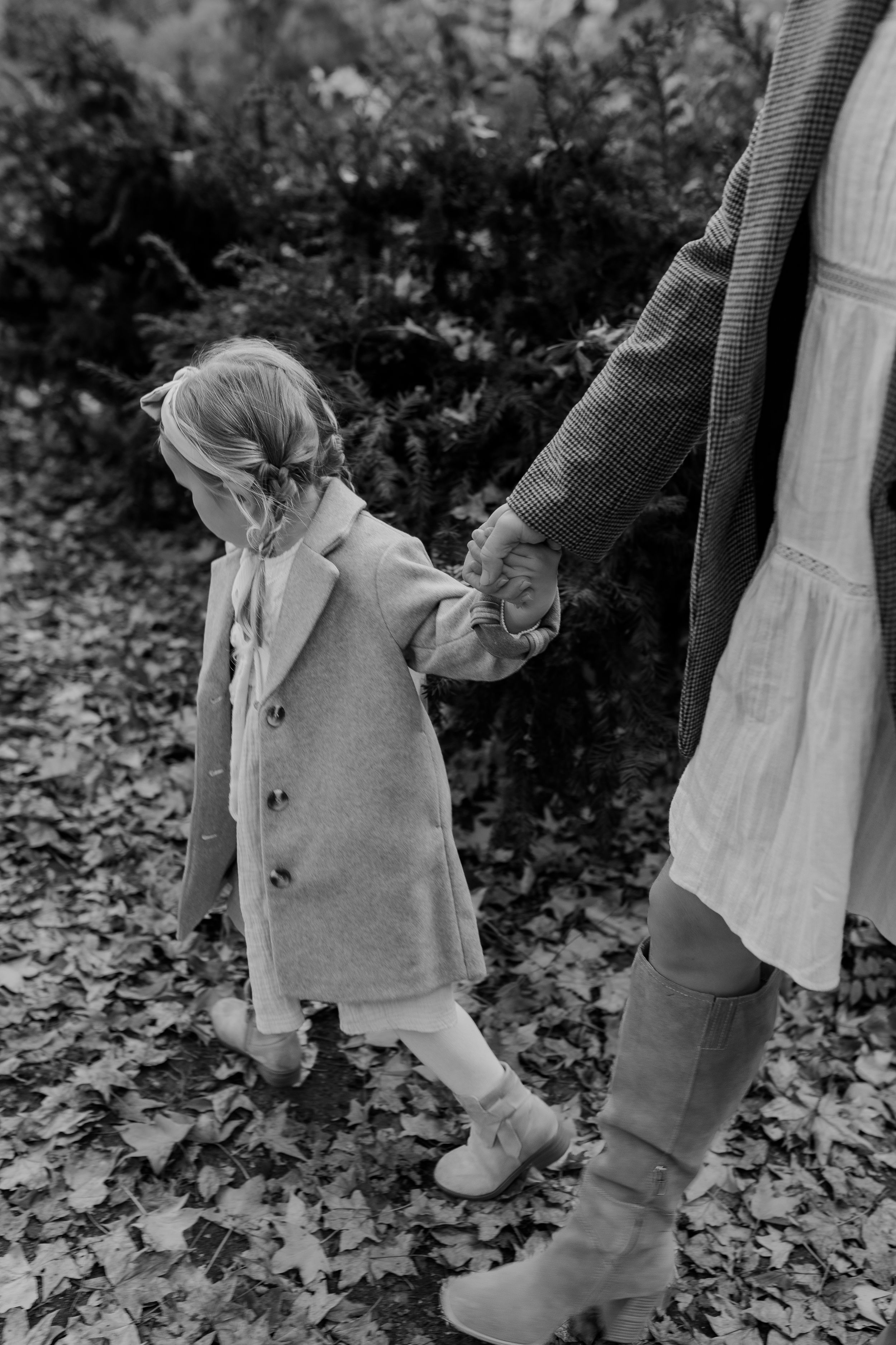 Black and white photo of two people walking through fallen leaves in autumn.