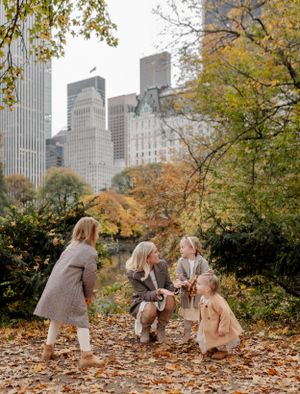 Group plays in fallen leaves with Manhattan skyline visible through autumn trees.