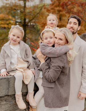 Family group poses on stone wall during autumn with fall foliage behind them.
