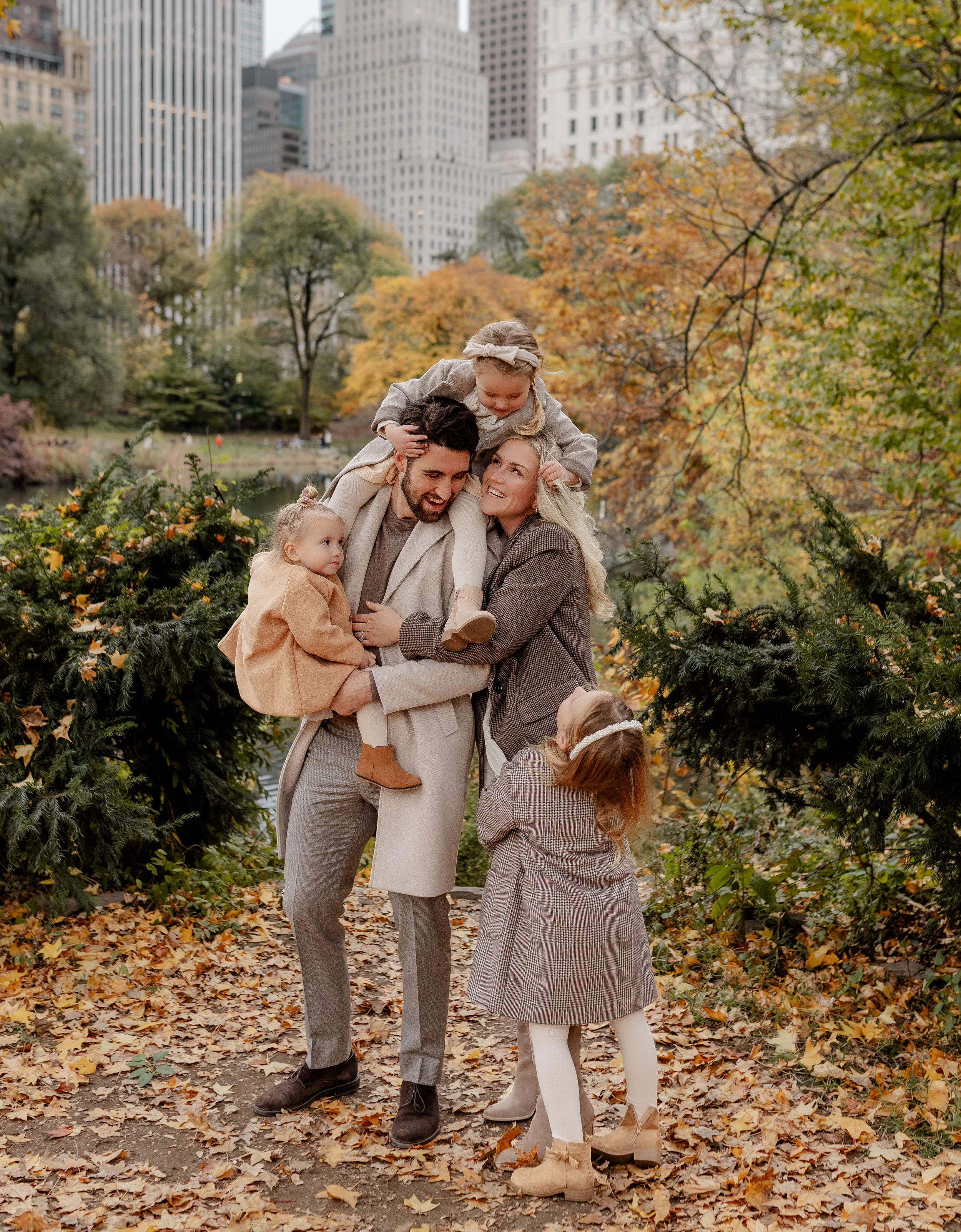 Family enjoying an autumn day in Central Park with city buildings in background.