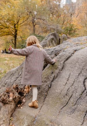 Child in plaid coat explores rocky terrain during autumn in park.