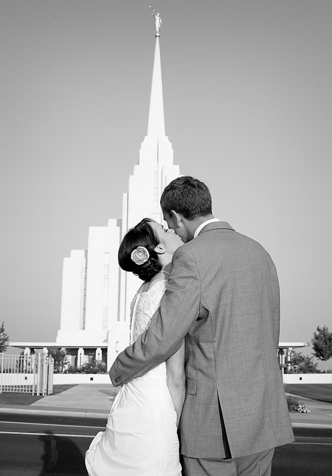 A couple embraces while looking at a white Mormon temple spire against a black and white sky.