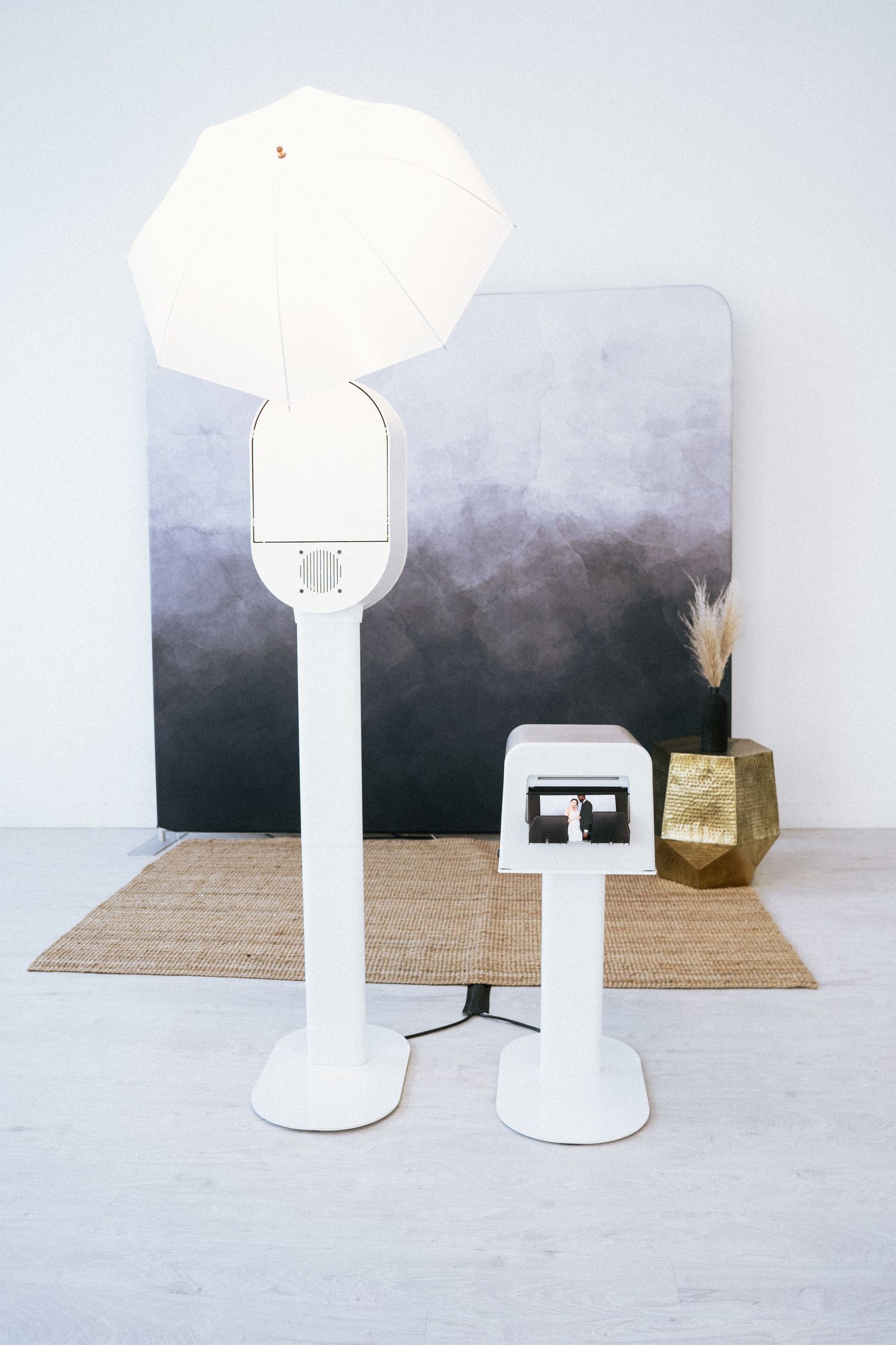 A minimalist photo booth with a round base and cylindrical shade shown from multiple angles on a wooden surface.