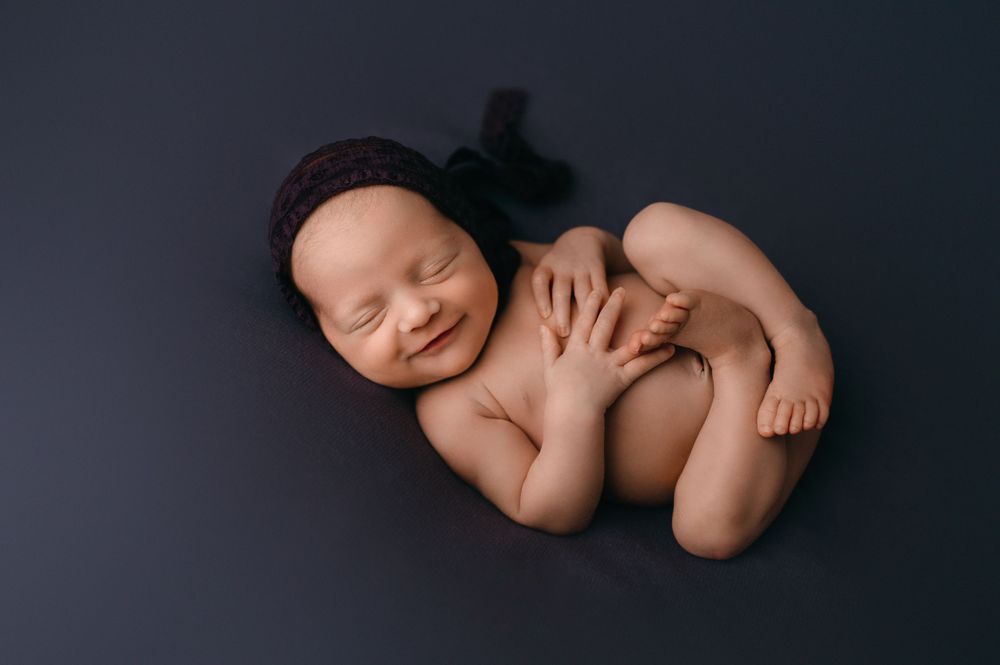 Peaceful newborn baby sleeping curled up on dark gray background in professional studio portrait.