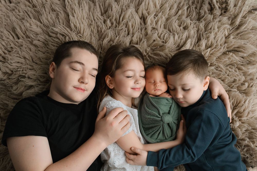 Four siblings snuggle close together while resting peacefully on a plush beige fur rug.