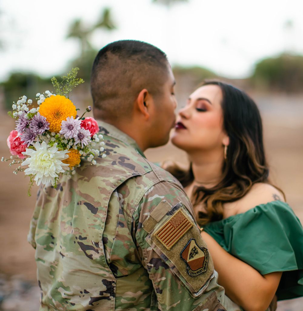 Military couple shares romantic moments in a garden with floral decorations and American flag patches.