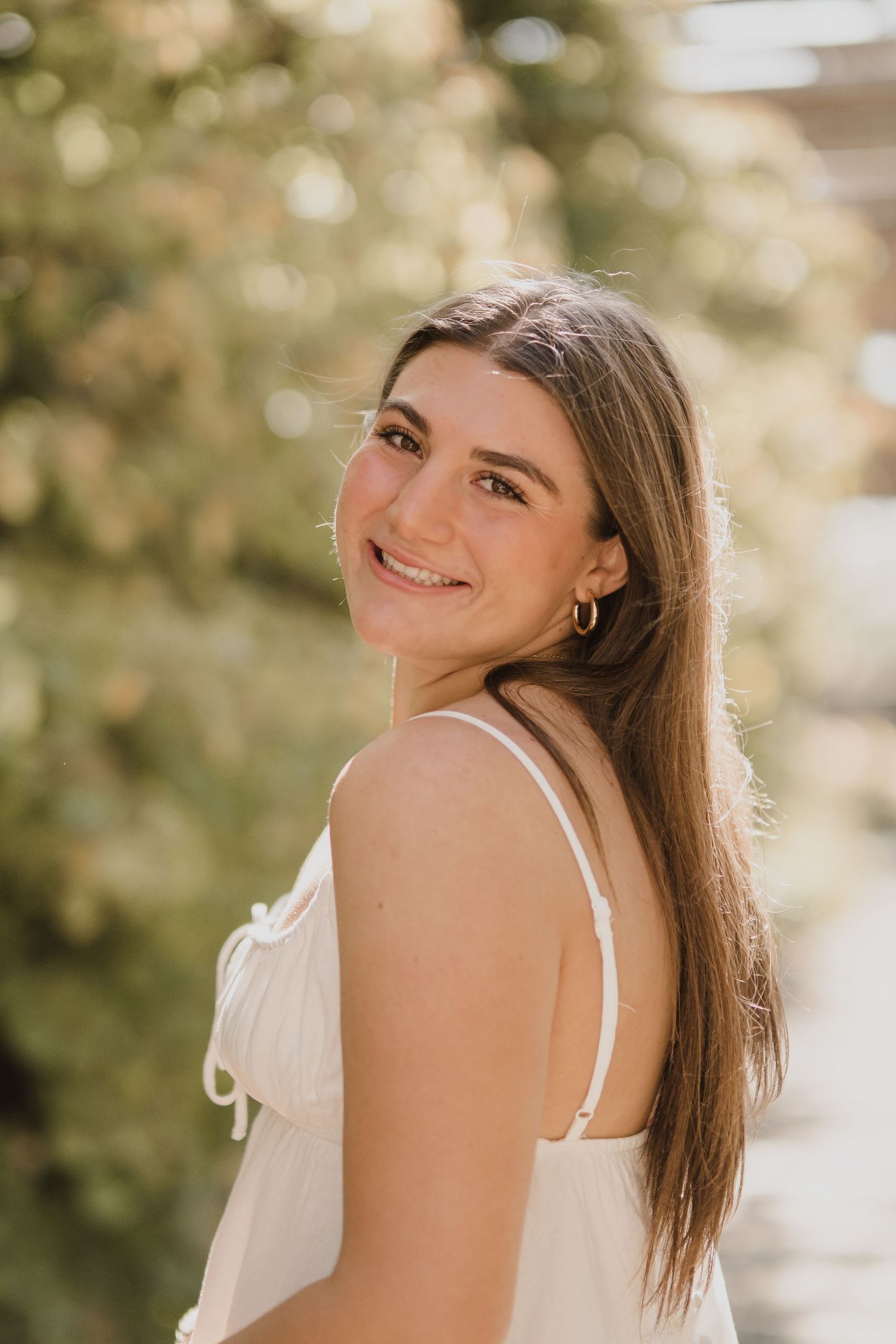 Person in white summer dress poses against soft bokeh nature background.