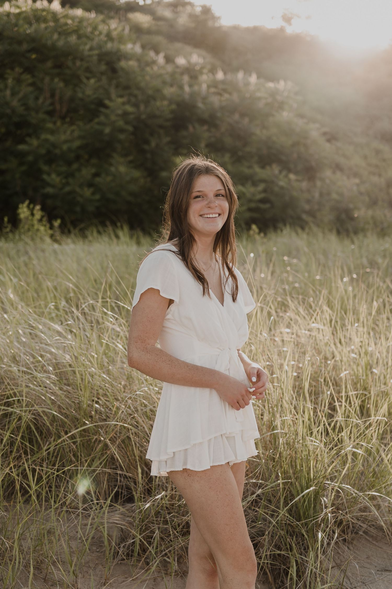 Person in white dress twirling playfully in a sunlit field.